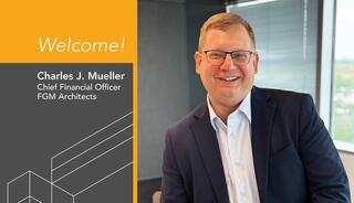 New FGMA CFO, Charles J. Mueller smiles in a suit, welcomes viewers with a warm expression in a modern office setting.