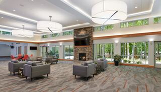 A modern multi-purpose gathering space featuring comfortable seating, a stone fireplace, and large windows offering views of nature, creating a cozy atmosphere.