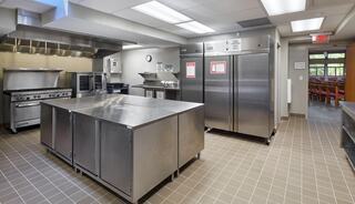 A commercial church kitchen featuring stainless steel appliances, a large prep island, commercial ovens, and multiple storage refrigerators.