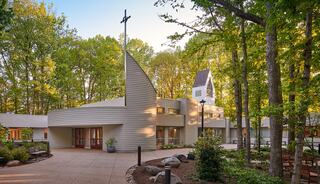 A modern church building, nestled among lush trees, featuring a prominent steeple and serene outdoor spaces.