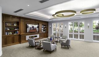 A church gathering space featuring comfortable seating, a large TV, bookshelves, and ample natural light from large windows, creating a welcoming atmosphere.