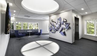 Second floor pf the rotunda features blue seating, an art installation, a skylight, and large windows showcasing greenery outside.