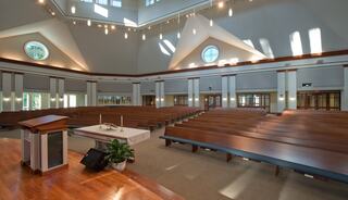 A spacious, well-lit interior of a church sanctuary, featuring wooden pews, an altar, and large windows that accentuate the architecture.