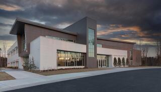 A modern church building features a blend of white and dark materials, large windows, and an open entrance, set against a dramatic sky.