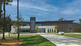 A modern church building features large windows with a cross, a mix of brick and stucco, landscaped grounds, and a paved driveway.