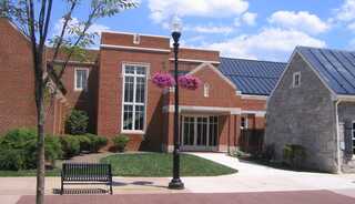 A brick church entry surrounded by greenery and a bench under a streetlight.