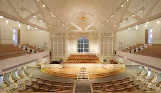A spacious, church sanctuary with tiered seating, an altar, and elegant lighting, creating a peaceful, uplifting atmosphere.