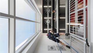 A person rappels down a sleek, modern vertical space, showcasing both windows and industrial design elements in a vibrant setting.