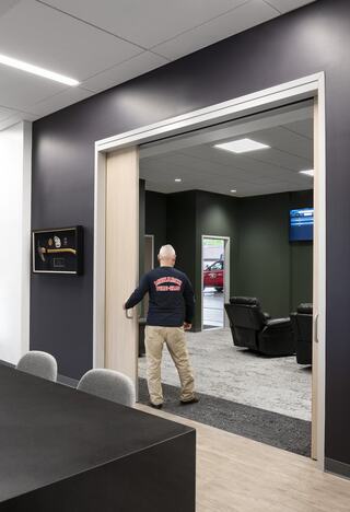 A person in a shirt walks through a doorway into a modern lounge area with recliners and a dark green wall.