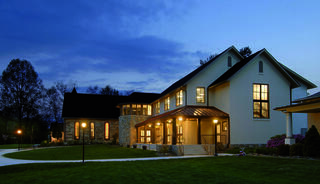 A renovated church building with large windows and warm outdoor lighting, set against a twilight sky and surrounded by a lush green lawn.