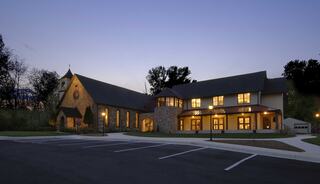 A renovated church building with stone and stucco, softly lit against a twilight sky, surrounded by a parking area.