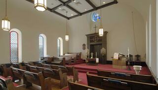 A church sanctuary featuring wooden pews, a central altar, stained glass windows, and warm lighting, creating a peaceful ambiance.