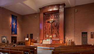 A church interior with reredos featuring wooden pews, and warm lighting.