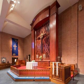 A church interior features a wooden reredos, a large cross backdrop, and elegant decor, creating a serene worship atmosphere.