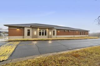 A modern one-story building features a mix of brick and stone exterior, set against a cloudy sky and surrounded by a grassy area.