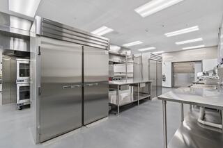 A modern kitchen featuring stainless steel refrigerators, open shelving, countertops, and a clean, organized layout. Bright, spacious environment.