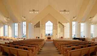 A modern, spacious sanctuary features wooden pews, large windows, and a softly lit altar area, creating a serene atmosphere for gatherings.