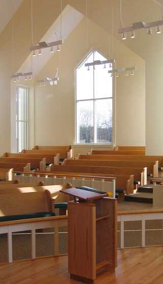 A modern worship space featuring wooden pews, large windows, and natural light, creating a serene and welcoming atmosphere.