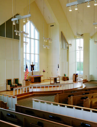 A spacious, modern sanctuary features high ceilings, large windows, an altar, and wooden pews, exuding tranquility and openness.