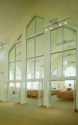 A spacious interior with tall, reflective windows, bright lighting, and wooden benches creates a serene atmosphere for gatherings.