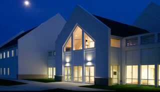 A modern church building with a peaked roof is illuminated at night, surrounded by dark blue sky and grass, creating a tranquil atmosphere.