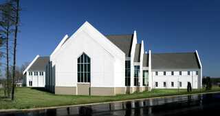 A modern church building features sharp angles and a mix of white and gray materials, set against a clear blue sky and green landscaping.