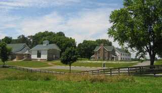 A picturesque church retreat center features two distinct buildings surrounded by lush greenery and a fence, under a bright blue sky.