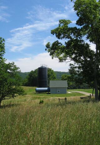 A sustainable church retreat features a a water tower surrounded by lush greenery and rolling hills under a blue sky with scattered clouds.