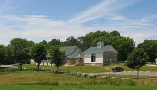 A serene chapel, multipurpose space and inn with stone front surrounded by lush greenery.