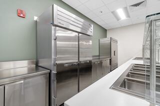 A sleek, modern kitchen featuring stainless steel refrigerators and a counter with multiple food prep sinks against a green wall.