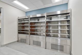 Three stainless steel display shelves with clear glass doors, set against a light-colored wall and tiled floor, appear empty and modern.