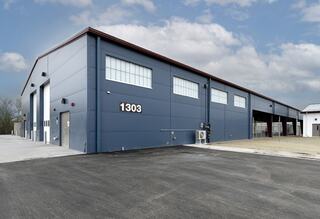 A modern blue industrial building with large windows and a concrete driveway, featuring a clear sky and minimal landscape.