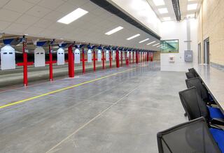 A spacious shooting range with multiple lanes marked by red supports, featuring a clean, modern design and a seating area along one side.