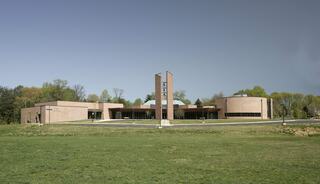 Our Lady of Good Counsel Catholic Church with brick exterior, large windows, set on a grassy area, surrounded by trees.