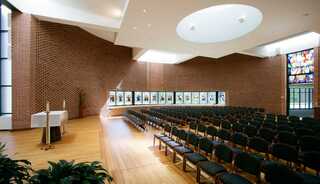 A serene worship space featuring wooden flooring, rows of chairs, and colorful stained-glass windows, highlighting a peaceful atmosphere.