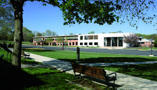 A church education wing with large windows, surrounded by green grass and trees, with benches lining the walkway.