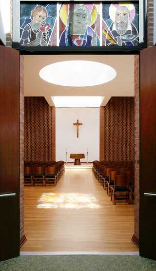 A serene chapel entrance features wooden doors, stained glass above, and a sunlit interior.