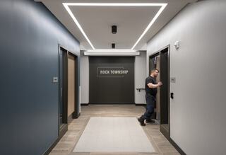 A modern hallway features sleek lighting, a sign for "Rock Township," and a person walking towards an elevator.