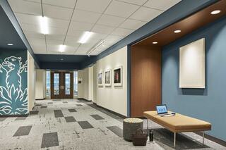 A modern hallway features textured carpet, a wooden bench with a laptop, framed artwork, and a decorative wall with vibrant patterns.