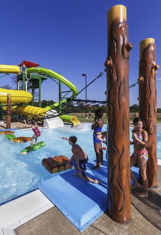 Children enjoy a water park with colorful slides and playful features, splashing in a pool under a clear blue sky.