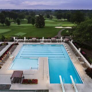 A tranquil swimming pool area with lounge chairs overlooks a lush golf course, surrounded by greenery under a softly lit sky.