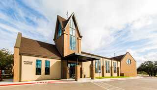 A worship center featuring a unique triangular roof, large windows, and a welcoming entrance set against a cloudy sky.
