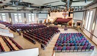 A spacious church interior with tiered seating, a central stage, and large windows providing natural light.