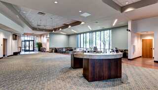 A spacious, modern gathering space featuring a reception desk, large windows, and ample seating. Brightly lit with a welcoming atmosphere.