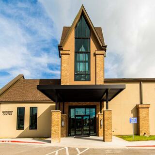 A church entry features a tall, pointed roof, large glass windows, and brick pillars, creating an inviting entrance.