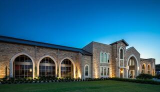 A stone church building with arched windows and a prominent entrance, beautifully illuminated against a twilight sky.