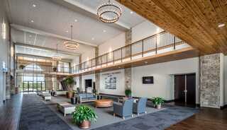 A modern fellowship space features high ceilings, elegant chandeliers, large windows, and comfortable seating surrounded by plants and stone accents.