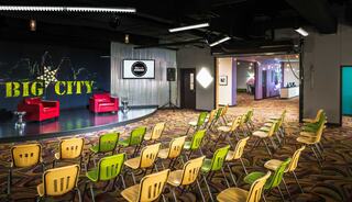 A vibrant auditorium space features red chairs on stage, bright yellow and green seating, and a colorful backdrop with "BIG CITY" displayed.