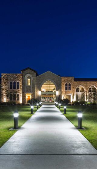 A well-lit pathway leads to a grand, stone church building, showcasing architectural elegance against a deep blue night sky.