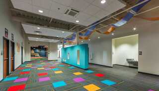 A vibrant hallway features colorful square carpets, teal walls, and playful decorations, creating a cheerful and inviting atmosphere.
